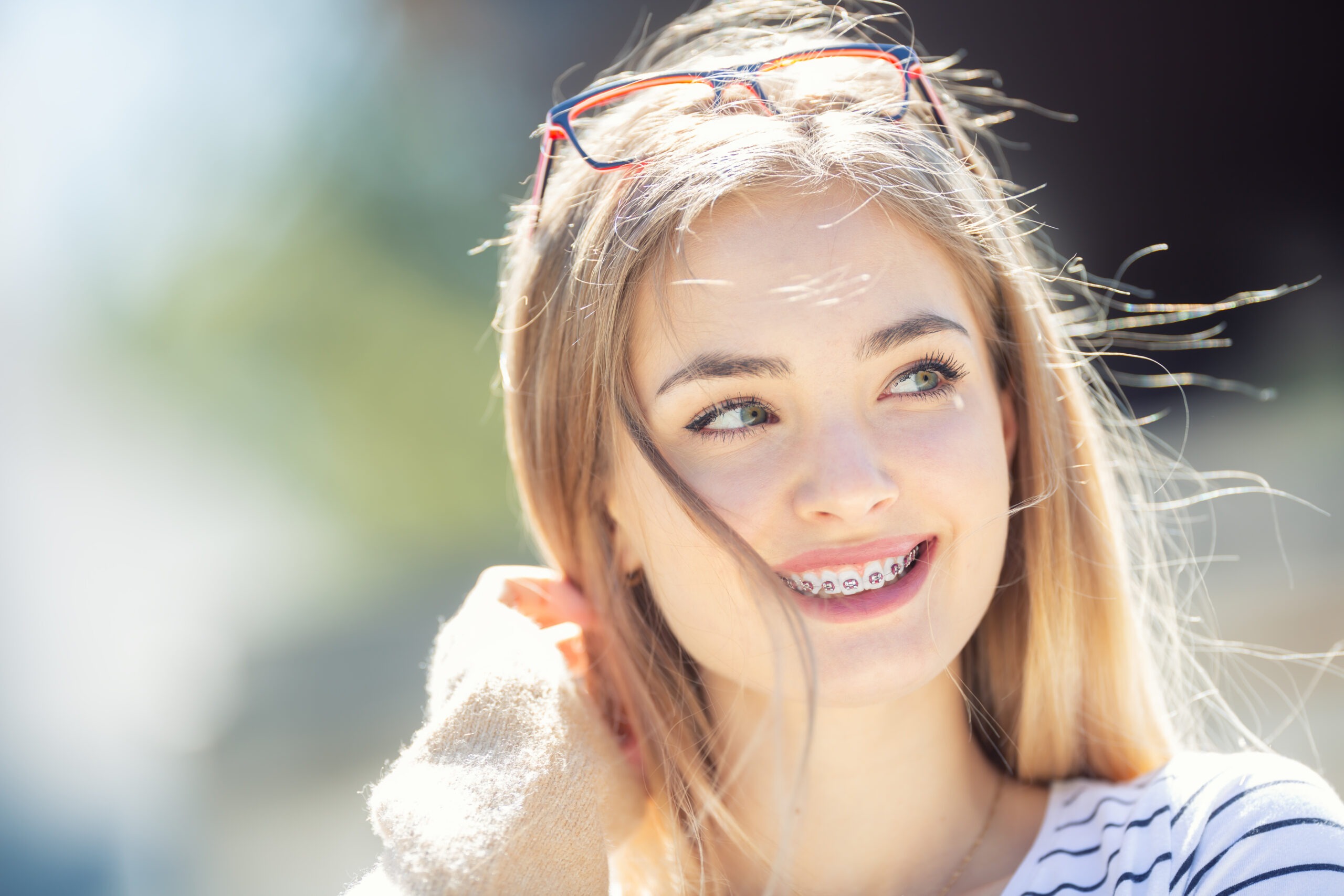 Smiling teen girl with glasses pushed up on her head in the sunshine, showing a confident smile from Ray + Swenson Orthodontics, orthodontist in Cedar Rapids