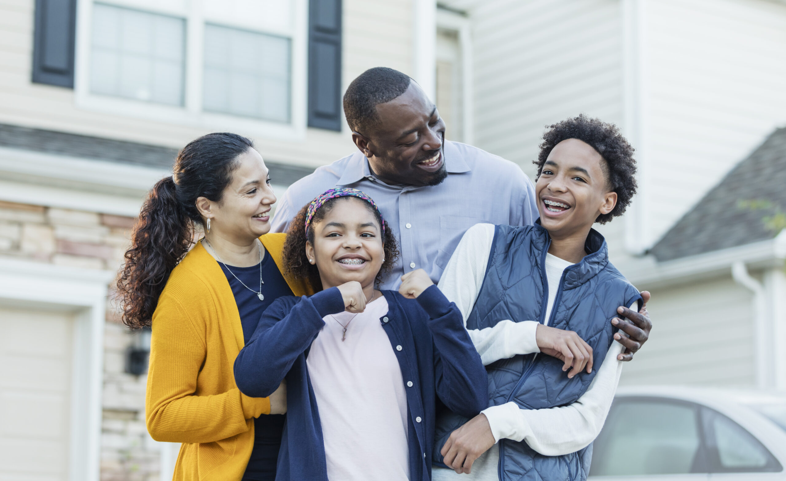 Happy family of five laughing together outside their home, celebrating healthy smiles with Ray + Swenson Orthodontics, orthodontist in Cedar Rapids